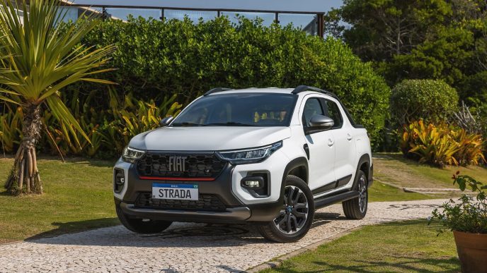 Fiat Strada 2025 branca, versão cabine dupla, estacionada em jardim tropical com fundo arborizado, destacando design robusto.