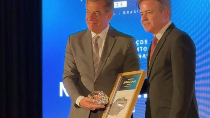 Nadim Elias Donato Filho recebe o Prêmio Aproxima Portugal–Brasil durante cerimônia no Porto, segurando troféu e certificado ao lado de representante da organização.