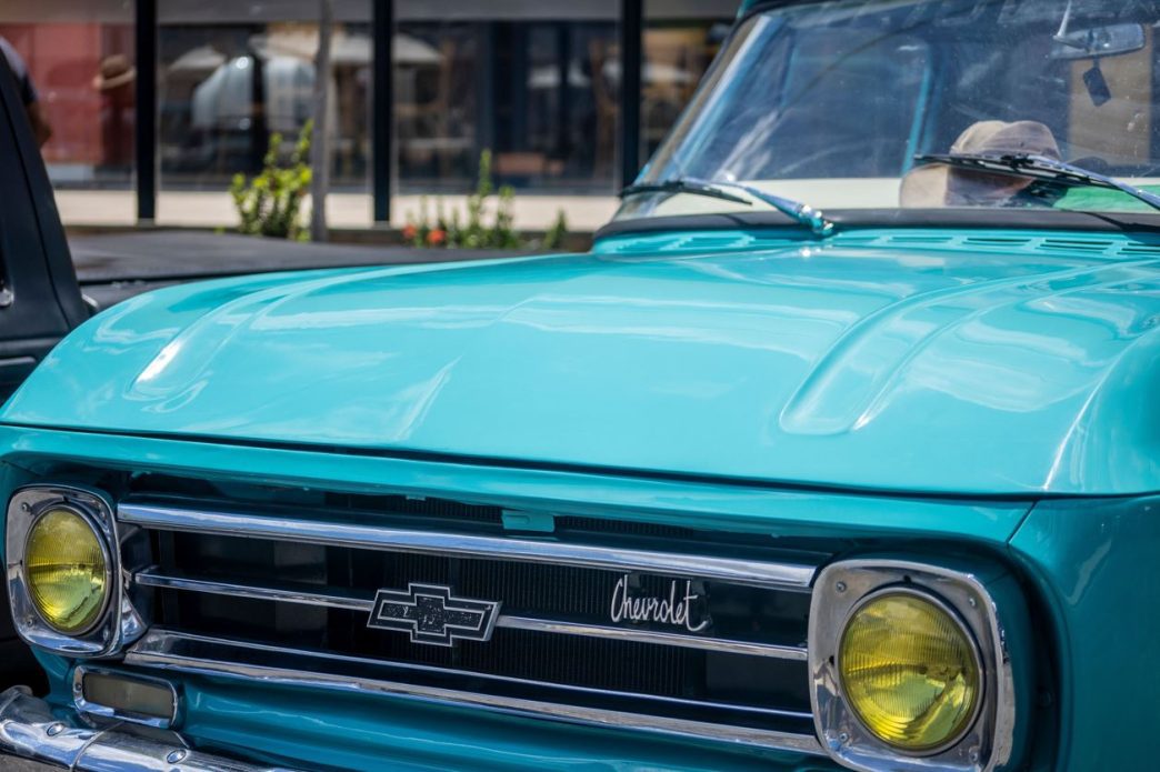 Frente de caminhonete clássica Chevrolet azul-turquesa com faróis amarelos, exposta em encontro de carros antigos no bairro Castelo, em Belo Horizonte.