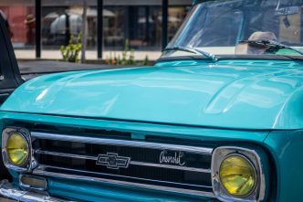 Frente de caminhonete clássica Chevrolet azul-turquesa com faróis amarelos, exposta em encontro de carros antigos no bairro Castelo, em Belo Horizonte.