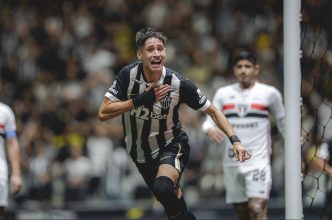 Jogador do Atlético comemora gol com expressão intensa na Arena MRV, enquanto atleta do São Paulo observa ao fundo durante partida do Brasileirão.