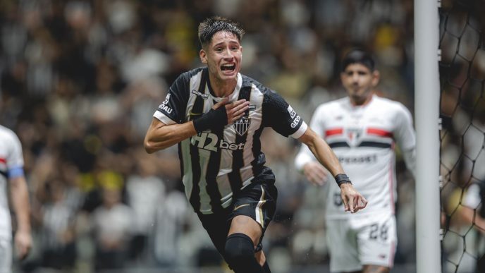 Jogador do Atlético comemora gol com expressão intensa na Arena MRV, enquanto atleta do São Paulo observa ao fundo durante partida do Brasileirão.