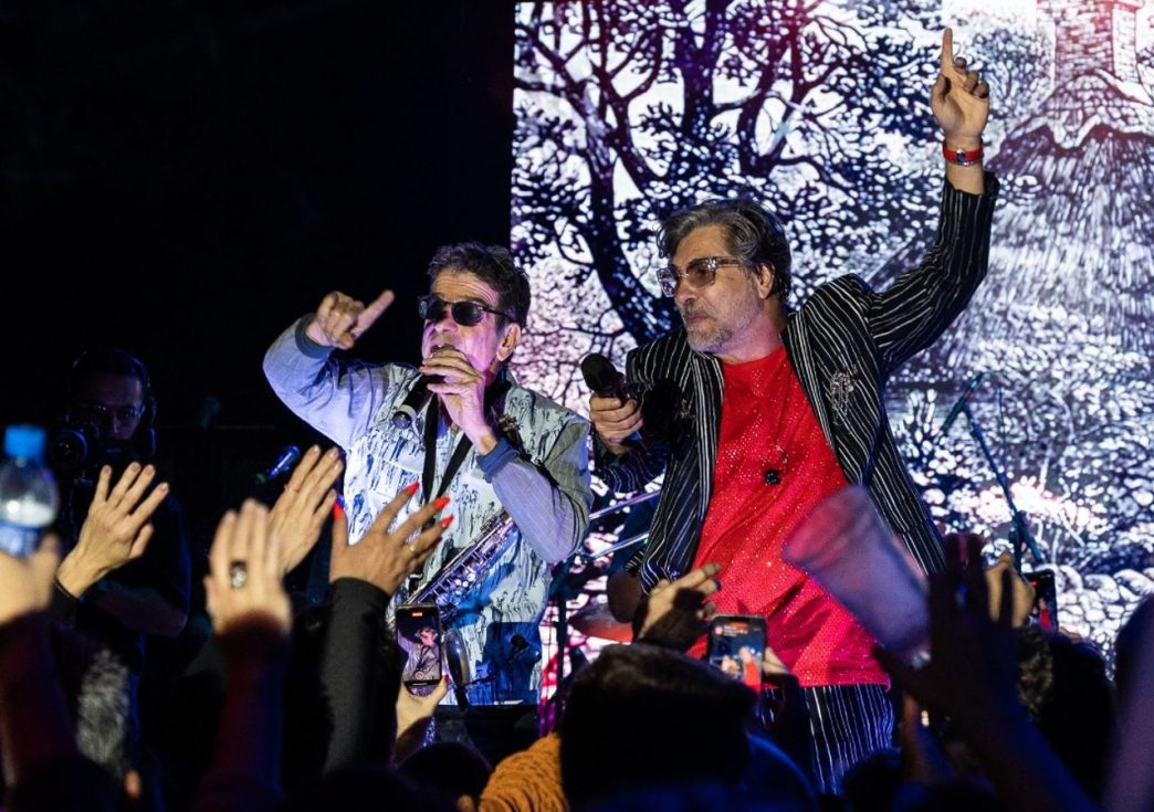 Fred Izak e George Israel se apresentam ao vivo no palco, interagindo com o público em show vibrante e cheio de energia.