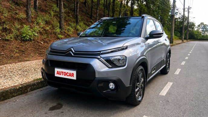 Vista dianteira em três quartos do Citroën C3 XTR 1.0 2026 na cor cinza, estacionado em via arborizada, destacando o visual aventureiro, rodas escurecidas e placa personalizada com a logomarca AUTOCAR.