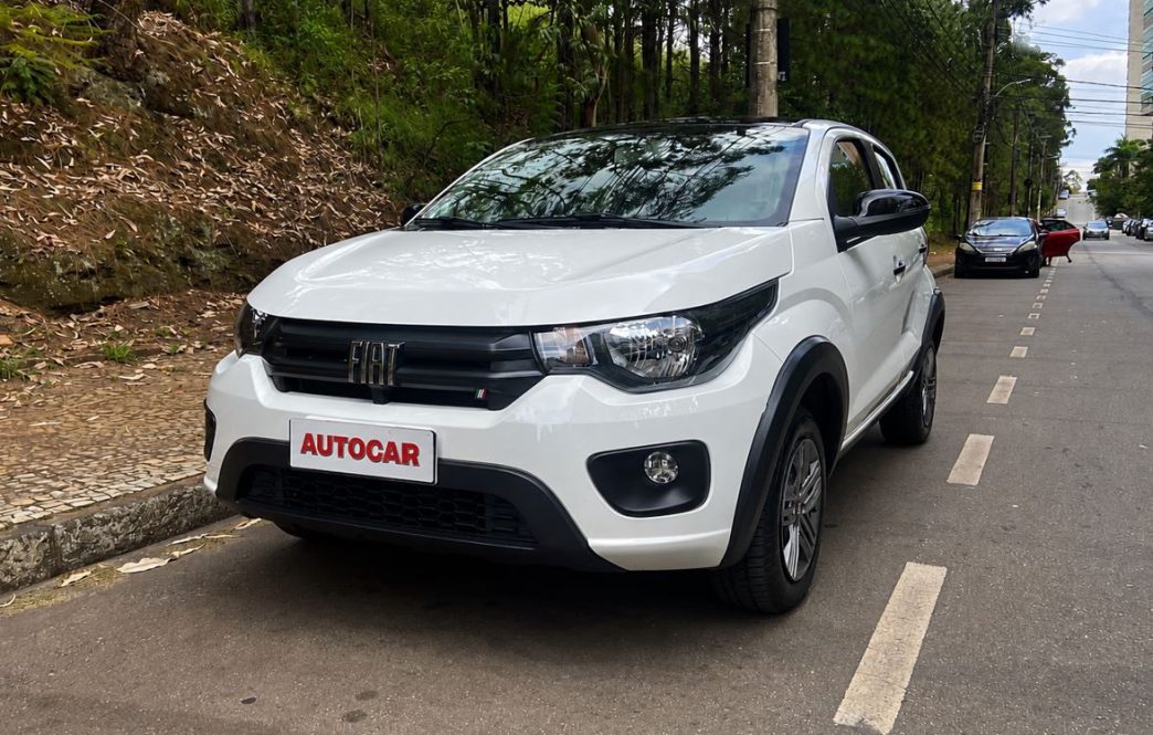 Fiat Mobi Like 2026 na cor branca estacionado em uma rua arborizada de Belo Horizonte durante avaliação realizada pela equipe da Autocar. O hatch compacto exibe a dianteira renovada, com detalhes em preto brilhante nos retrovisores e maçanetas, além da placa personalizada com a logomarca Autocar.
