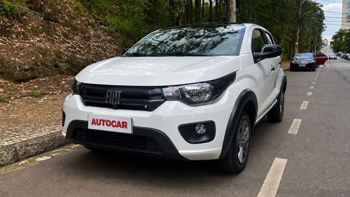 Fiat Mobi Like 2026 na cor branca estacionado em uma rua arborizada de Belo Horizonte durante avaliação realizada pela equipe da Autocar. O hatch compacto exibe a dianteira renovada, com detalhes em preto brilhante nos retrovisores e maçanetas, além da placa personalizada com a logomarca Autocar.