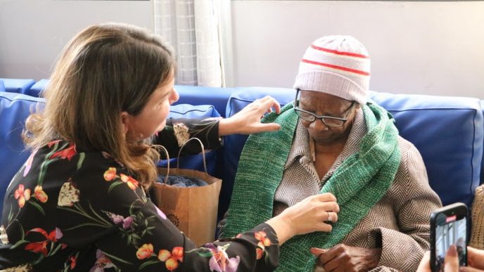 Mulher entrega cachecol verde a idoso durante ação solidária da campanha Calor Humano do Servas em Belo Horizonte.