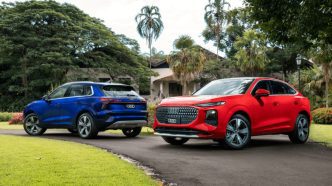 Audi Q3 Sportback vermelho e Audi Q3 azul estacionados em área arborizada, destacando o novo design da terceira geração dos SUVs premium da marca alemã.