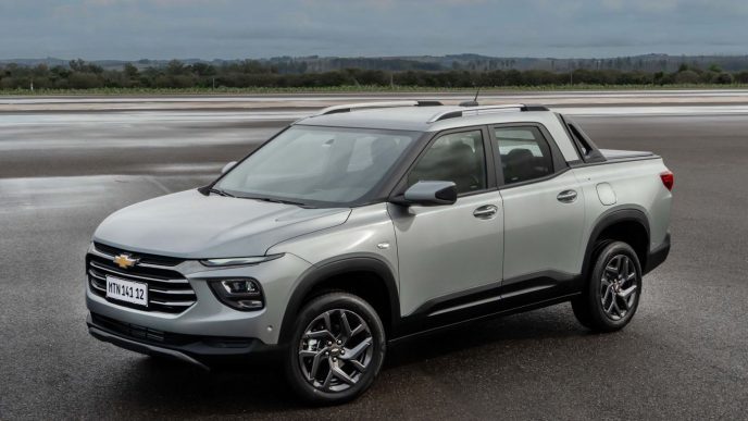 Chevrolet Montana 2027 prata em pista molhada, vista de frente e lateral, destacando visual de SUV com caçamba, rodas de liga leve, rack de teto e Santo Antônio integrado.