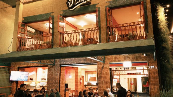 Fachada iluminada do Ô Chefe Steakhouse em Belo Horizonte, com clientes sentados nas mesas externas durante a noite.