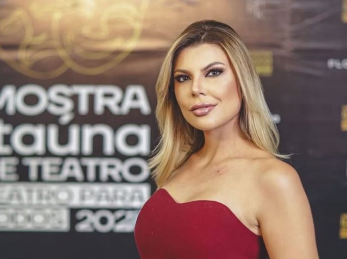 Mulher loira usando vestido vermelho posa em frente a painel de evento, com expressão confiante, representando matéria sobre comunicação e oratória em Belo Horizonte.