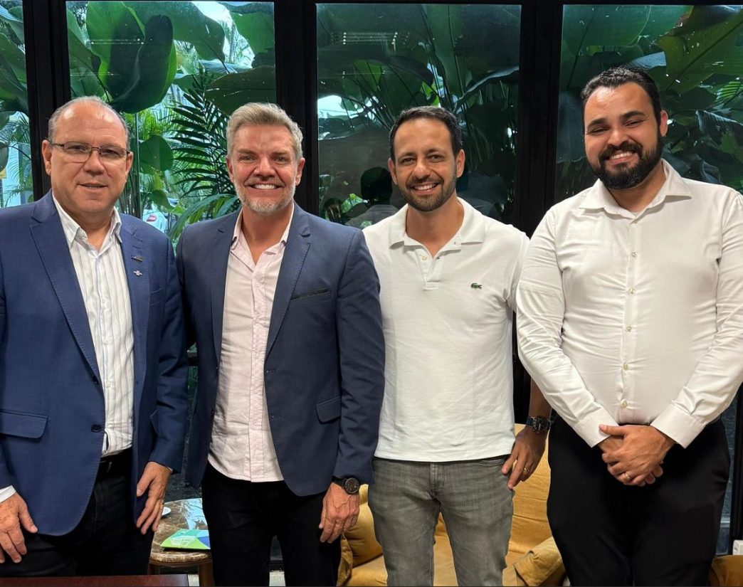 Quatro homens sorridentes em escritório com plantas ao fundo