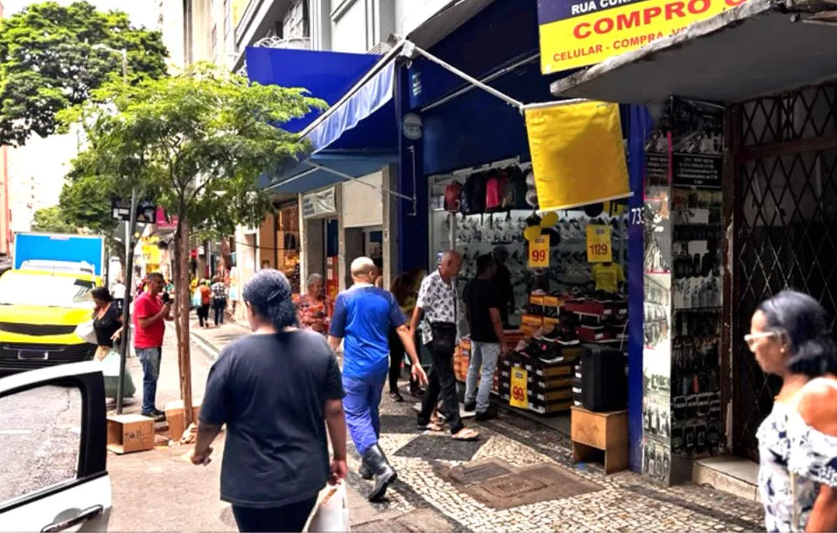 Pessoas caminhando em calçada movimentada com lojas.