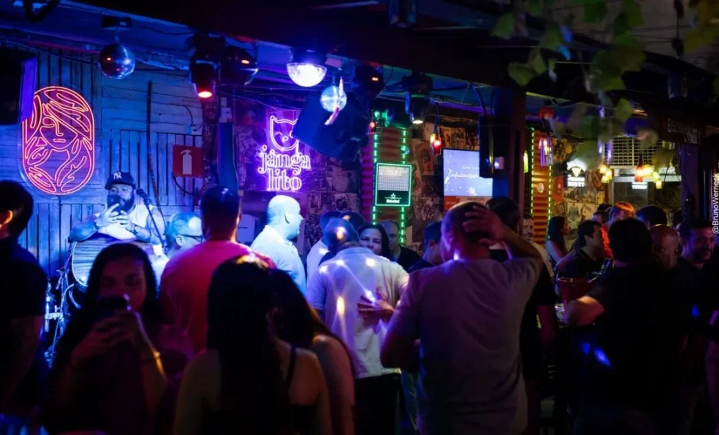 Público lota o Jangal, em Belo Horizonte, durante evento noturno com música ao vivo, iluminação de neon e clima descontraído, destacando a cena cultural vibrante da capital mineira.