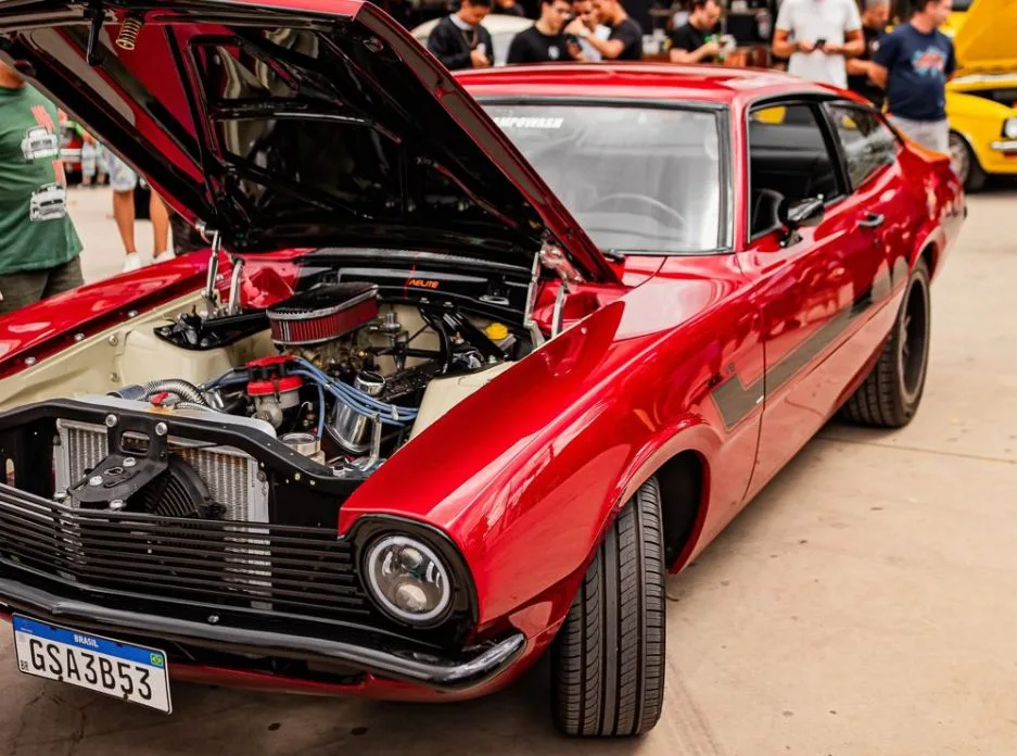 Ford Maverick GT V8 vermelho com capô aberto, exibindo motor preparado em destaque durante exposição no maior encontro de carros antigos de Minas Gerais, no Parque das Mangabeiras, em Belo Horizonte, cercado por visitantes admirados.