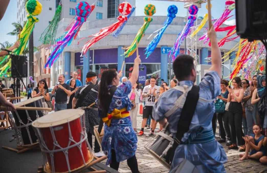 Apresentação de taiko durante o Festival Tanabata Matsuri em Belo Horizonte, com músicos em trajes tradicionais japoneses tocando tambores, cercados por público atento e enfeites coloridos pendurados, representando a tradicional celebração da cultura nipônica.