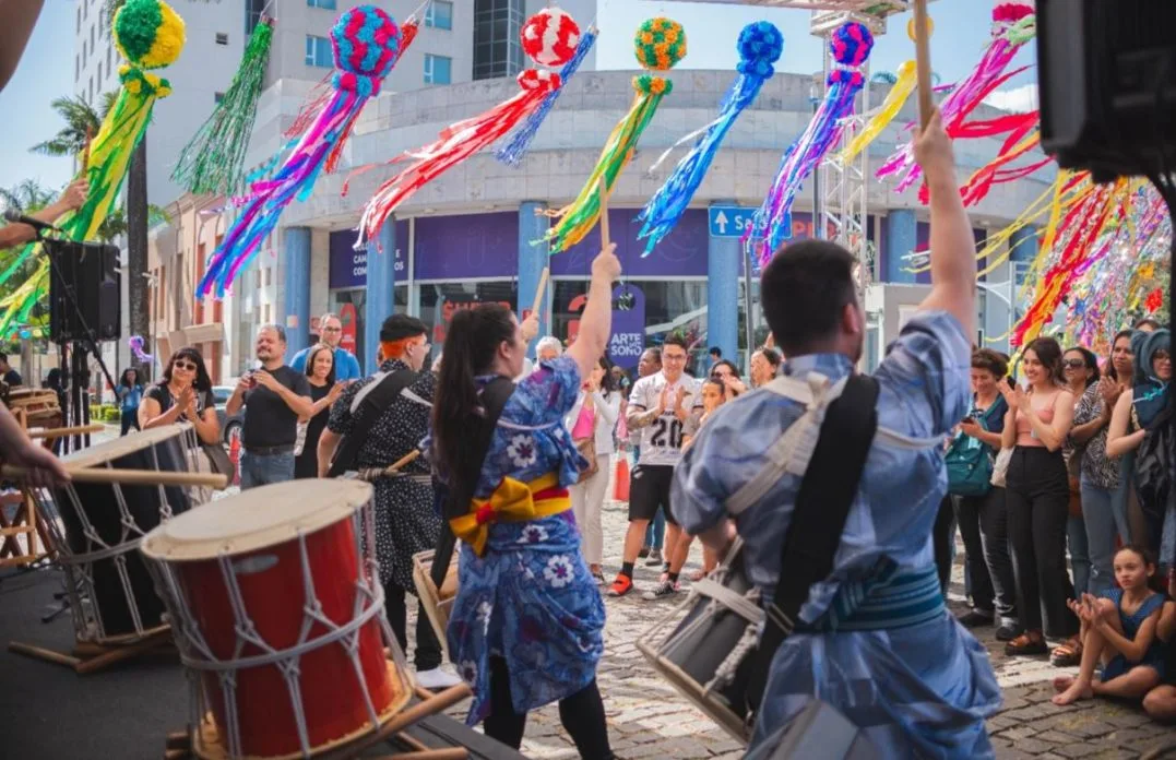 Apresentação de taiko durante o Festival Tanabata Matsuri em Belo Horizonte, com músicos em trajes tradicionais japoneses tocando tambores, cercados por público atento e enfeites coloridos pendurados, representando a tradicional celebração da cultura nipônica.