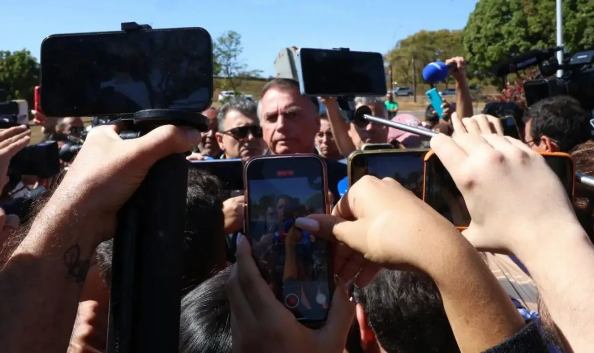 Jair Bolsonaro cercado por jornalistas e apoiadores durante entrevista coletiva em espaço público, sendo registrado por dezenas de celulares e câmeras, em meio a repercussões sobre imposição de tornozeleira eletrônica determinada pelo STF.