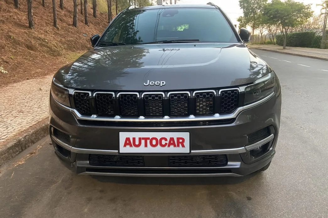 Frontal do Jeep Commander Overland 2025 com motorização 2.2 Turbodiesel, destacando a grade de sete fendas clássica da Jeep, faróis full LED e placa personalizada da Autocar, durante teste em ambiente urbano arborizado.