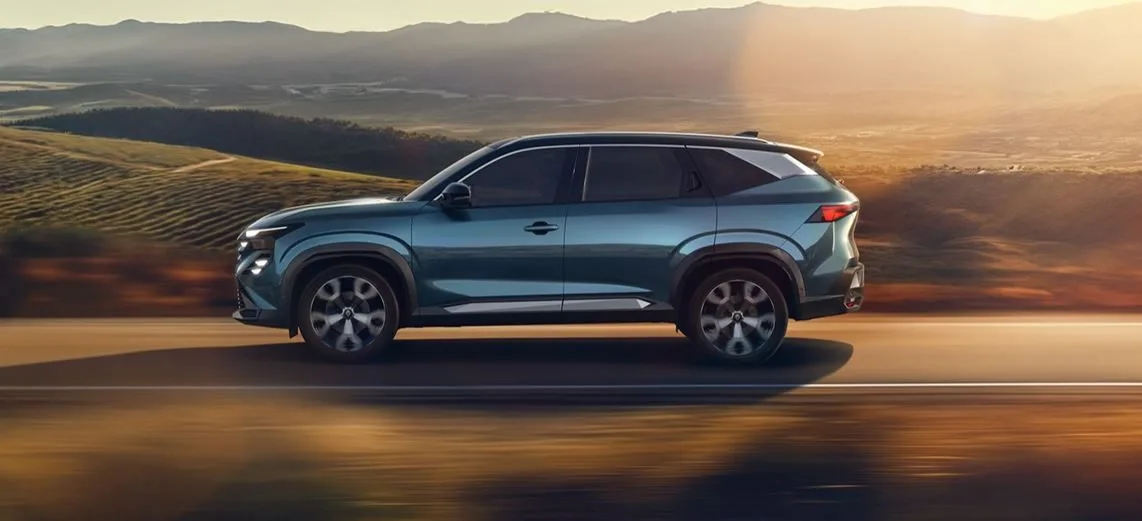 Renault Boreal 2025 em movimento sobre estrada aberta ao entardecer, SUV azul metálico visto de perfil com paisagem montanhosa ao fundo.