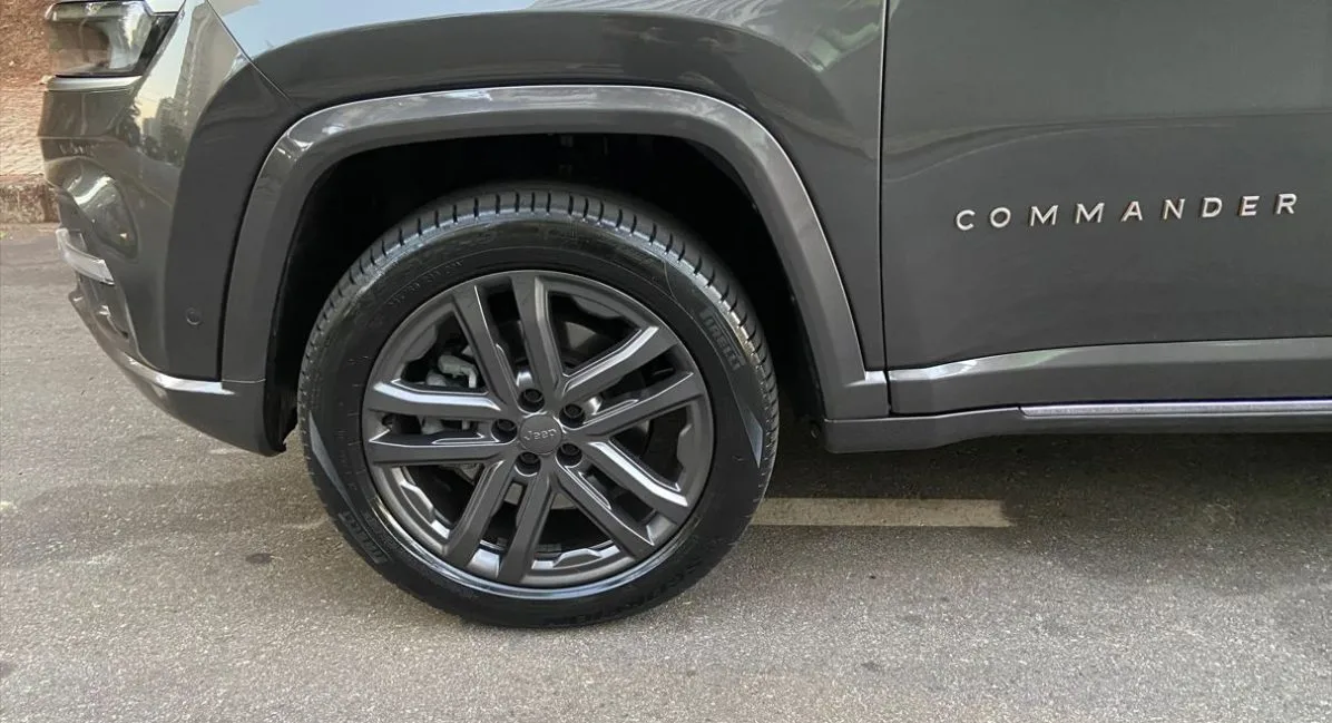 Detalhe da roda dianteira do Jeep Commander Overland 2025 com aro de liga leve escurecido, pneus Pirelli de perfil alto e acabamento cromado nos para-lamas, exibindo o emblema 'Commander' na lateral da carroceria.