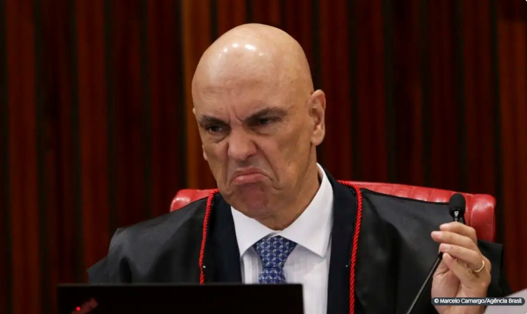 Ministro Alexandre de Moraes, do STF, com expressão severa durante sessão no plenário, vestindo toga e segurando caneta.