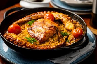 Prato Arroz Atlântico do Bar All Mar, servido em panela de ferro, com salmão grelhado, polvo, tomate, arroz temperado e ervas.