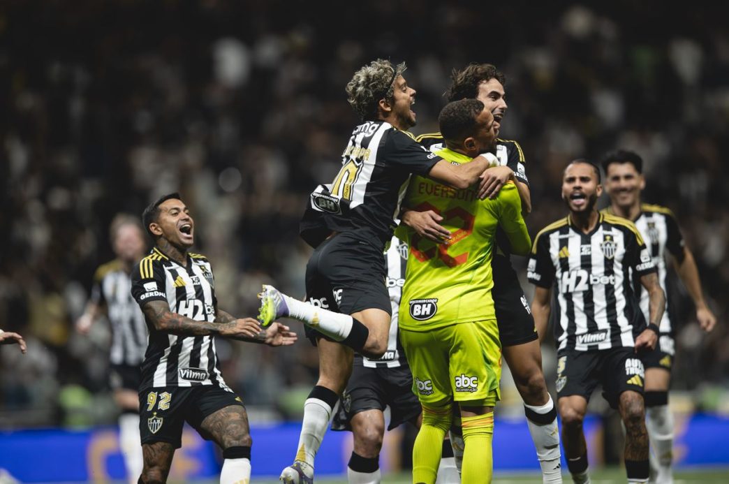 Jogadores do Atlético Mineiro comemoram efusivamente a classificação sobre o Flamengo, com Everson sendo abraçado no centro da imagem após marcar o pênalti decisivo, enquanto companheiros vibram com intensidade no gramado da Arena MRV.
