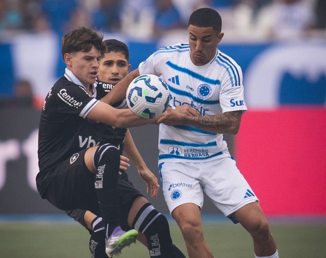 Jogador do Cruzeiro disputa a posse de bola com dois atletas do Botafogo durante partida intensa no estádio Nilton Santos, pelo Brasileirão 2025.