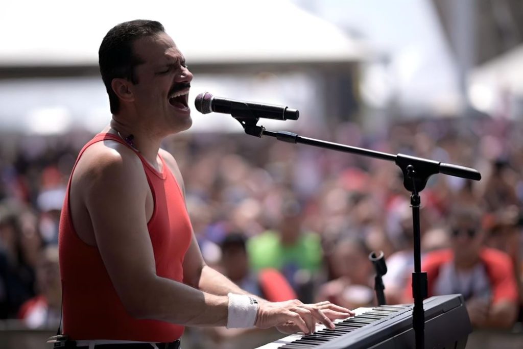 Vocalista da banda Lurex se apresenta ao vivo no Bop Games, cantando e tocando teclado diante de um público atento e vibrante.