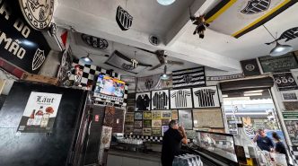 Interior do Bar do Salomão em Belo Horizonte, decorado com bandeiras, escudos e camisas do Clube Atlético Mineiro, com ambiente boêmio e elementos históricos nas paredes, incluindo televisão ligada, clientes ao balcão e iluminação tradicional.