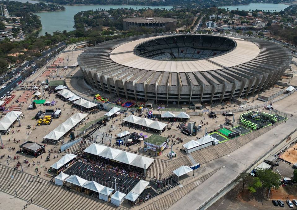 Vista aérea do estádio Mineirão, em Belo Horizonte, durante evento esportivo e cultural, com tendas, arenas e público distribuído na Esplanada Sul.