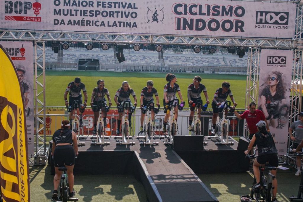 Instrutores e participantes pedalam em bicicletas estacionárias durante aula de ciclismo indoor no gramado do Mineirão, no Bop Games.