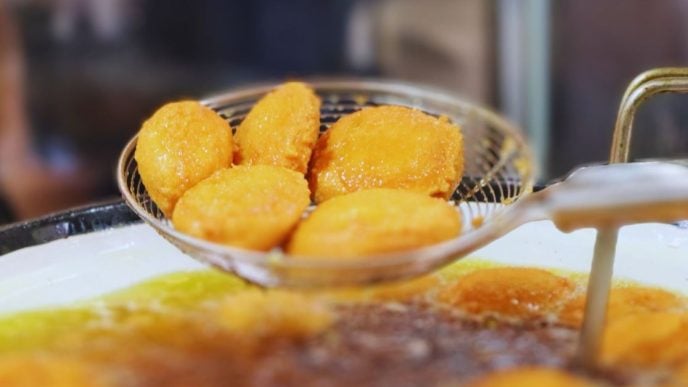 Acarajés dourados sendo escorridos do óleo em peneira metálica durante preparo típico nordestino na Feira Gastronômica de Santa Tereza.