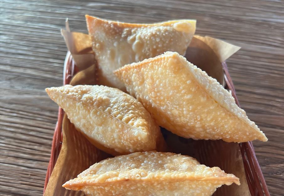 Cesta de madeira com minipastéis fritos, dourados e crocantes, dispostos sobre papel manteiga, sobre mesa de madeira rústica.