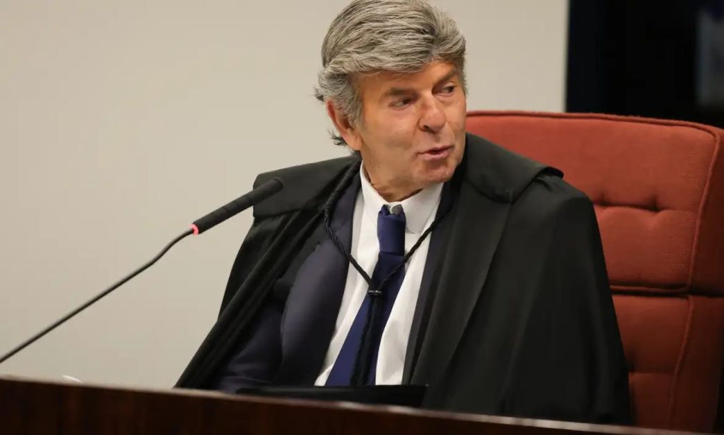 Ministro Luiz Fux, do STF, sentado na cadeira do plenário, usando toga preta e falando ao microfone durante sessão da Corte.