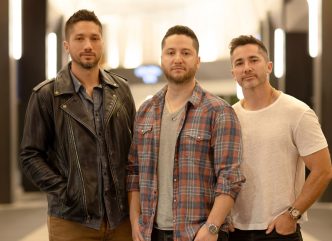 Os irmãos Alejandro, Fabian e Daniel Manzano, da banda Boyce Avenue, posam lado a lado em ambiente interno iluminado, promovendo turnê no Brasil com show confirmado em Belo Horizonte.