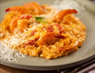 Prato de risoto cremoso com camarões salteados, tomatinhos confit e lascas de parmesão, servido em prato de cerâmica.