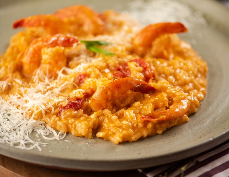 Prato de risoto cremoso com camarões salteados, tomatinhos confit e lascas de parmesão, servido em prato de cerâmica.