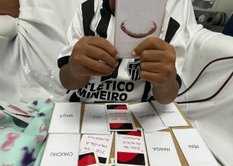 Criança em tratamento na Santa Casa BH segura carta educativa com imagem de alimento, durante atividade psicopedagógica no ambulatório.