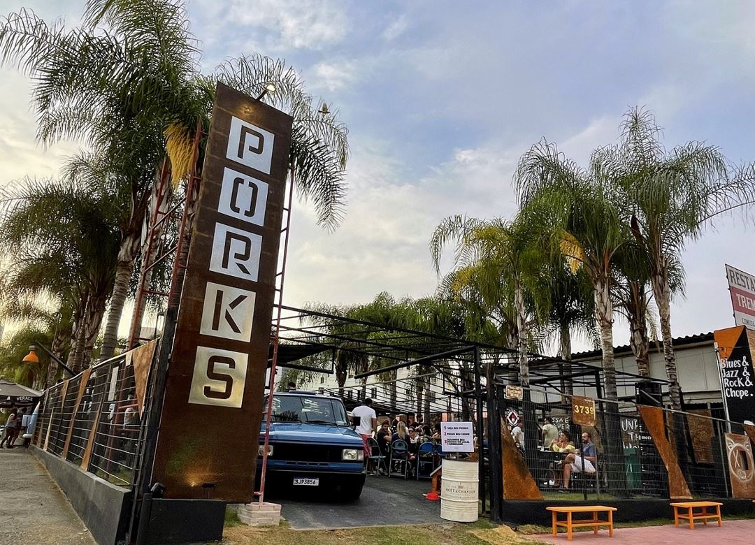 Fachada do Porks Castelo em Belo Horizonte, com placa vertical em destaque, palmeiras ao fundo e público reunido para o evento.