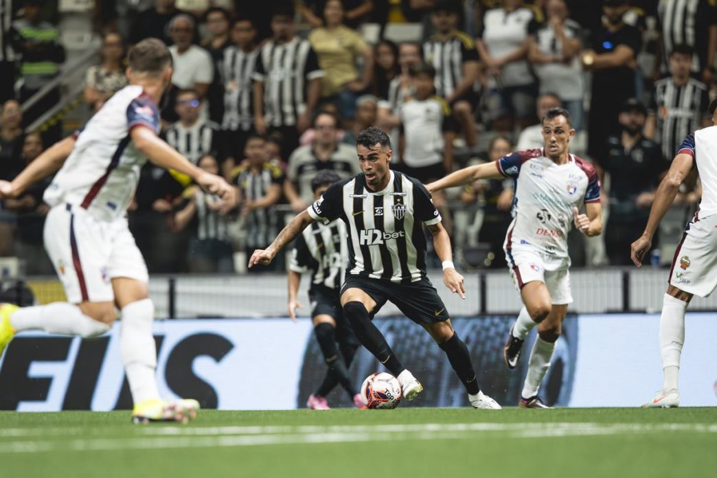 Jogador do Atlético Mineiro conduz a bola durante partida contra o Betim na Arena MRV, cercado por marcadores, sob os olhares da torcida.