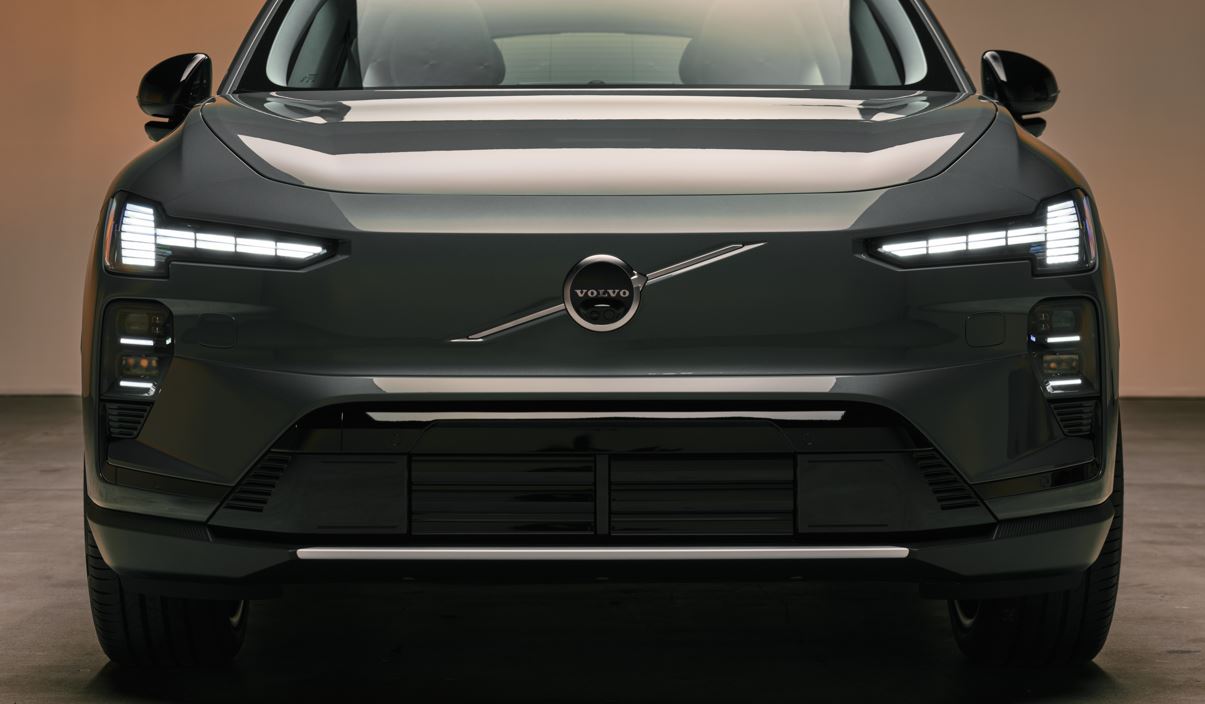 Vista frontal do Volvo EX60 destacando grade aerodinâmica, faróis em LED com assinatura luminosa em “T” e logotipo central da Volvo.