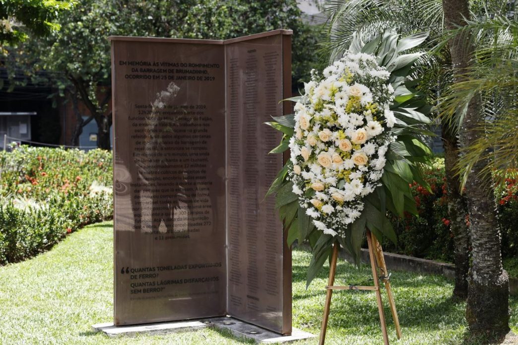 Monumento em homenagem às 272 vítimas da tragédia de Brumadinho, ladeado por uma coroa de flores brancas e amarelas.