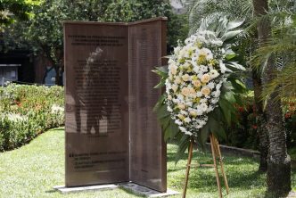 Monumento em homenagem às 272 vítimas da tragédia de Brumadinho, ladeado por uma coroa de flores brancas e amarelas.