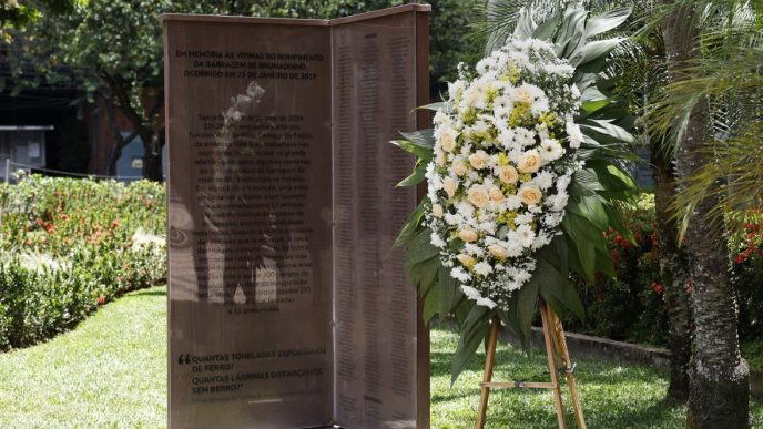 Monumento em homenagem às 272 vítimas da tragédia de Brumadinho, ladeado por uma coroa de flores brancas e amarelas.