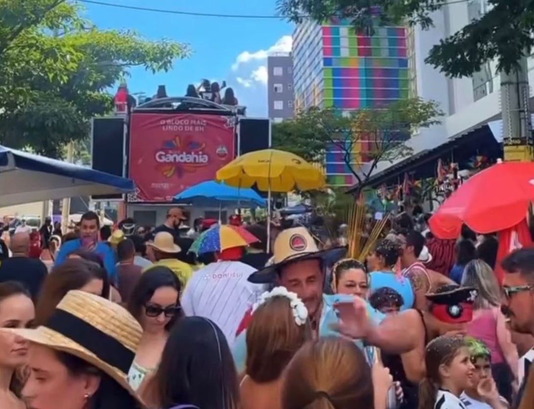 Multidão animada celebra o Carnaval em Belo Horizonte durante o desfile do Bloco Gandahia, com trio elétrico ao fundo e foliões fantasiados.