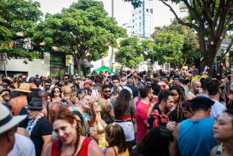Multidão de foliões durante bloco de rua do Carnaval em Belo Horizonte, sob árvores e luz do dia, em clima de festa e diversidade.