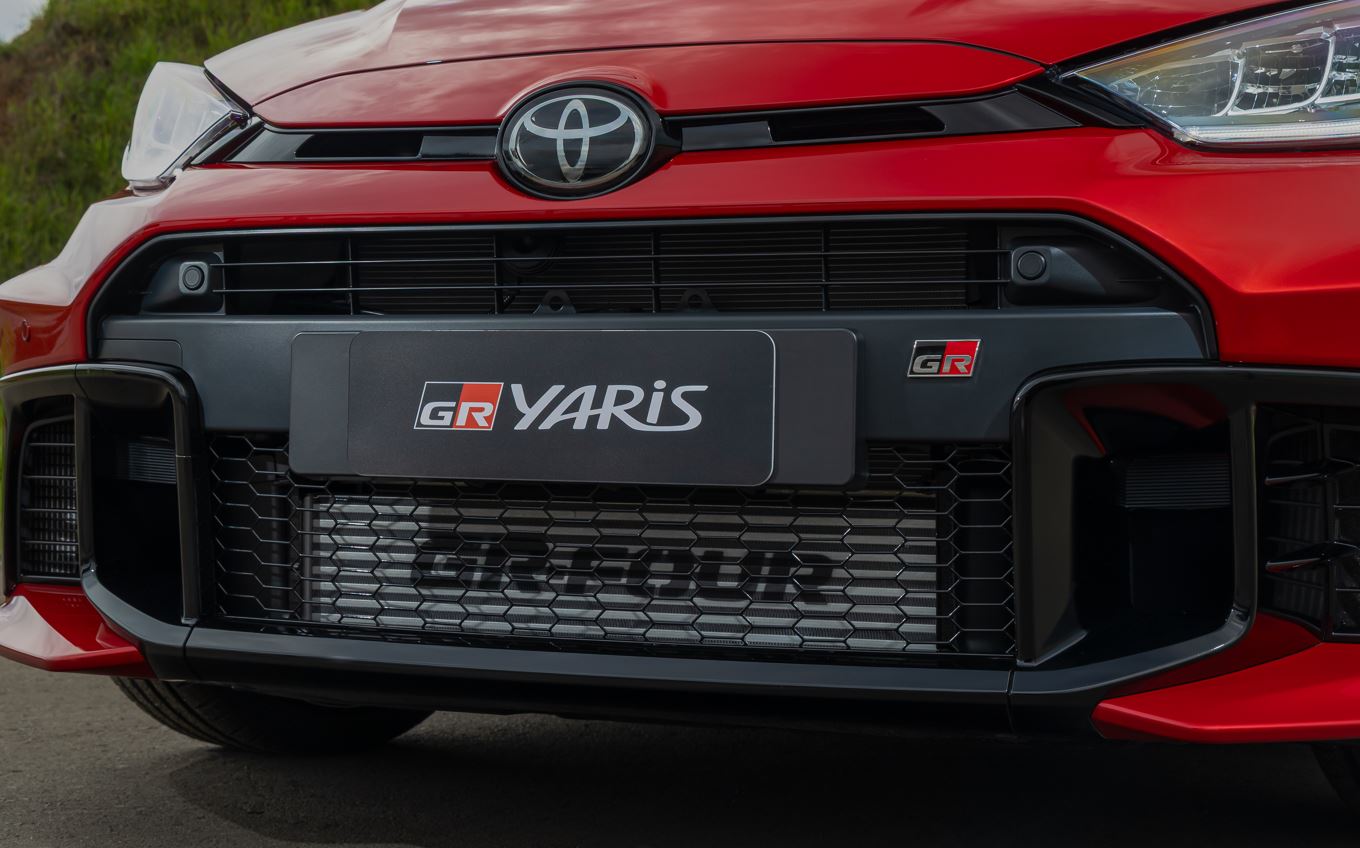Detalhe da dianteira do Toyota GR Yaris vermelho, destacando grade frontal ampla em colmeia, logotipo Toyota, emblema GR e faróis afilados em LED.