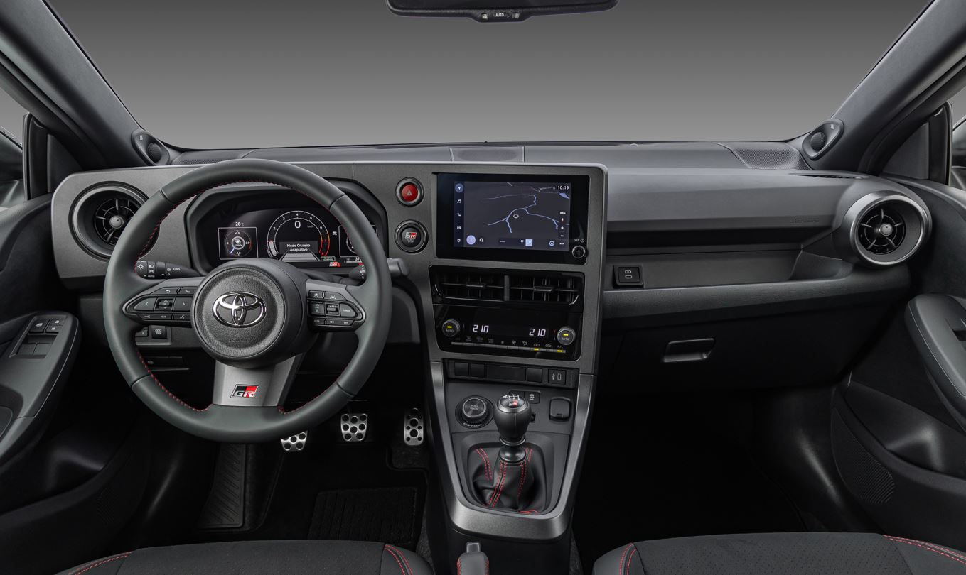 Painel do Toyota GR Yaris com volante multifuncional GR, quadro de instrumentos digital, central multimídia touchscreen e câmbio manual com acabamento esportivo.